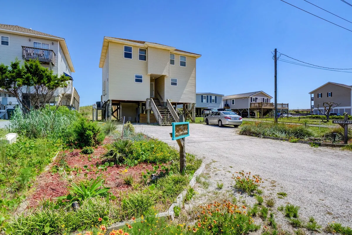 This exterior shot captures the vacation rental home with its landscaped garden, visible parking area, and neighboring homes. The image emphasizes the ease of arrival and shows the dedicated parking that guests will enjoy.