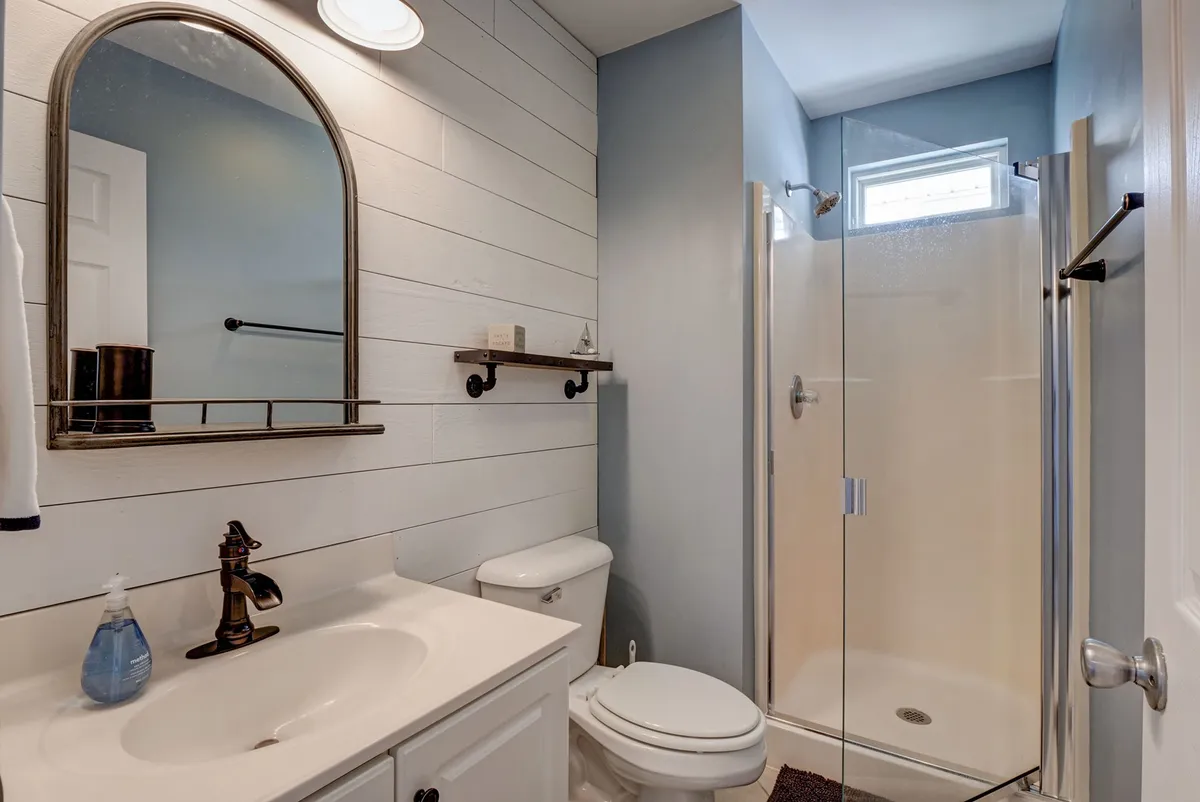 A bright, clean bathroom with a mirror, shower, sink, and toilet. The space feels fresh and inviting, ideal for personal routines and relaxation after a day at the beach.
