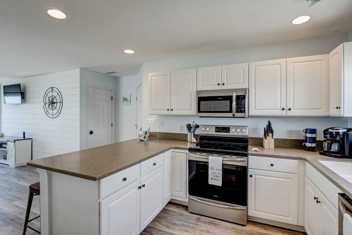 A modern kitchen with a central island, stainless steel appliances, and white cabinetry. The space feels bright and functional, inviting guests to cook, entertain, or simply enjoy a meal together.