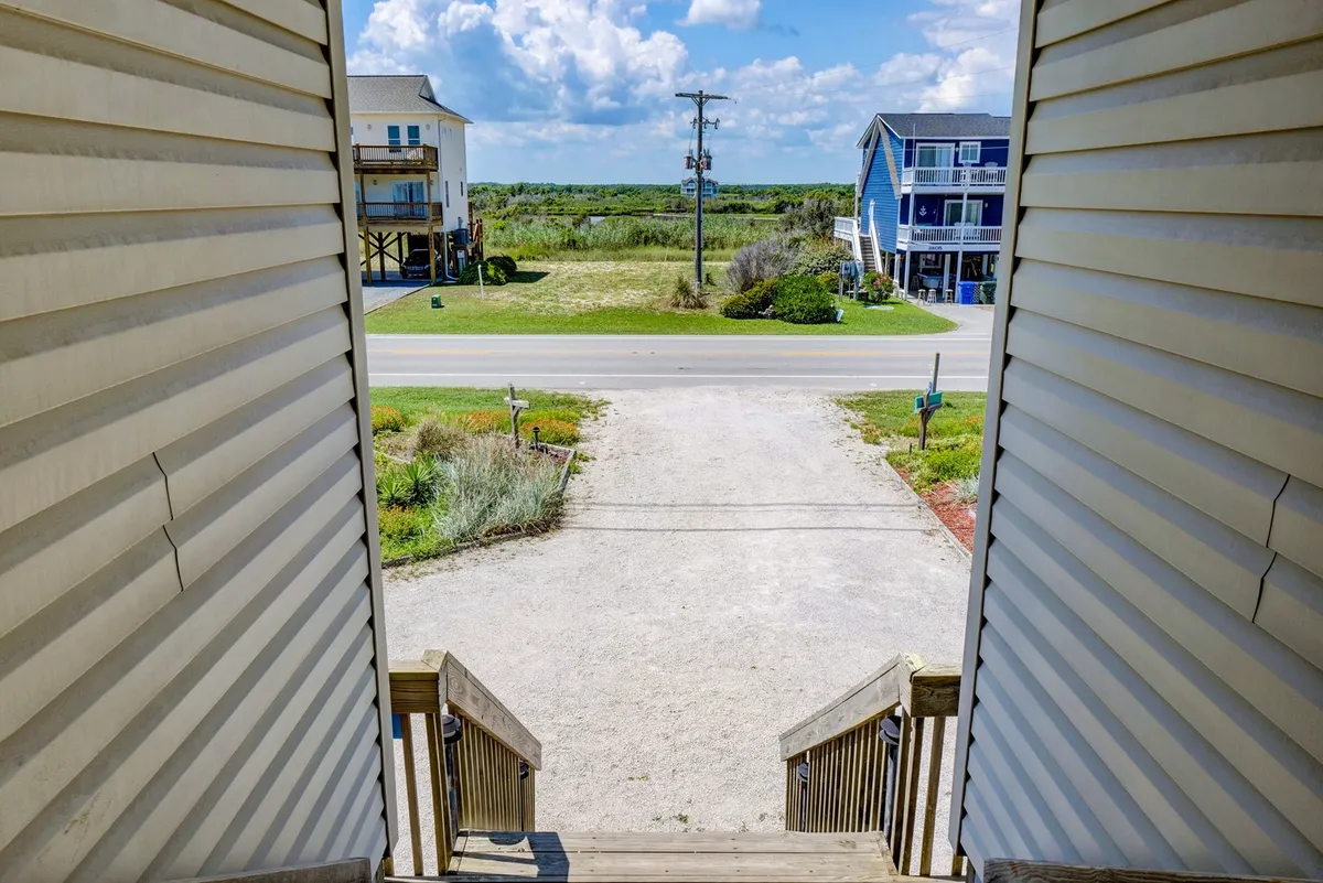 An exterior viewpoint from a deck or staircase, overlooking a quiet neighborhood with a road, greenery, and houses. The relaxed setting hints at the proximity to local attractions and easy access to morning walks or coffee shop outings.