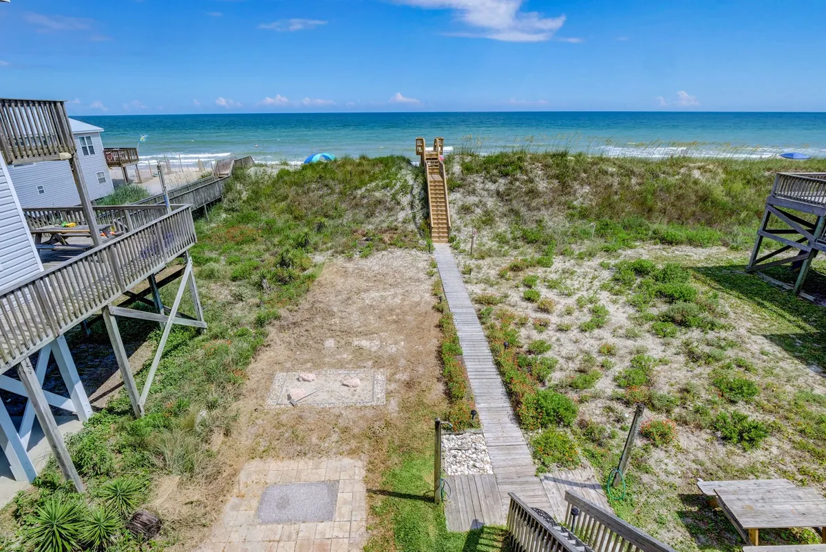The image features beach access stairs leading down to the ocean, surrounded by lush greenery and a patio area—an inviting transition between the home and the sand. The view hints at the convenience and exclusivity of private beach access, while also suggesting space for family gatherings and outdoor meals.