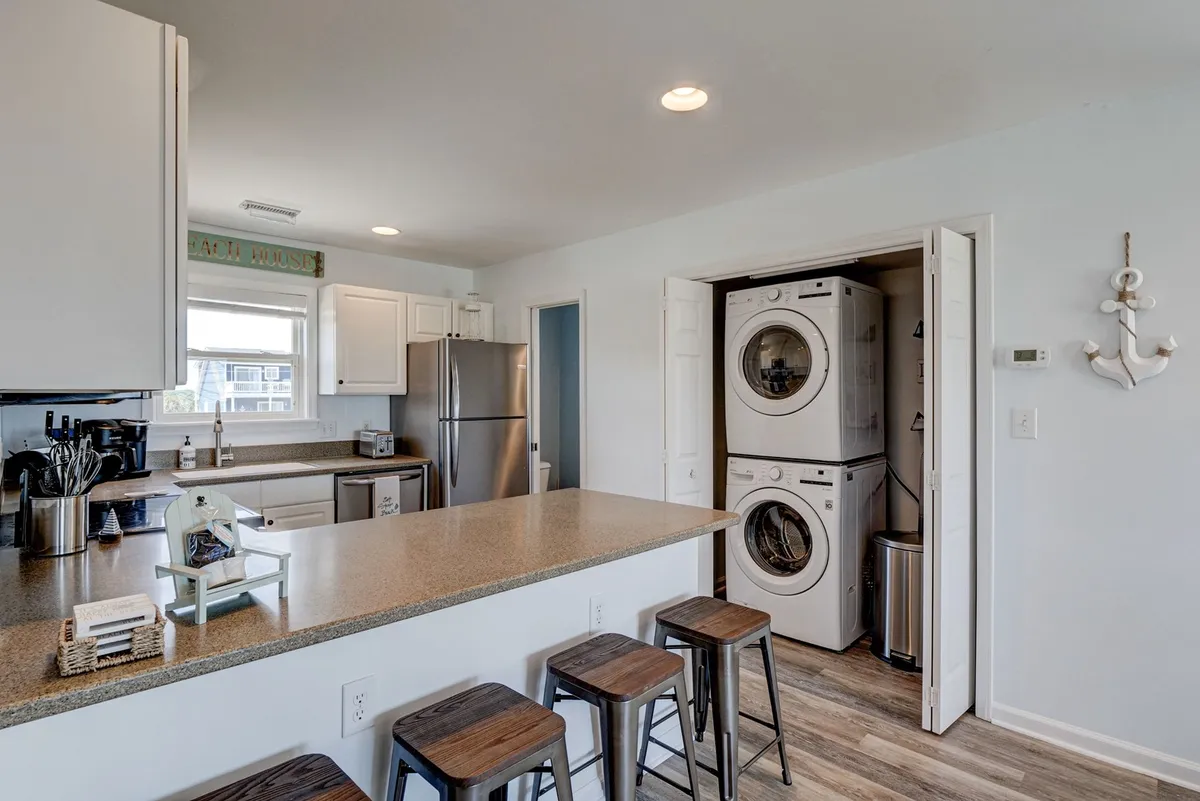 This interior scene features a functional laundry area adjacent to the kitchen, with a visible washer and dryer and practical cabinetry. The space is bright, organized, and clearly designed for easy post-beach cleanups.